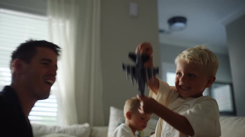 A father plays with his two toddler sons in the living room all having a great time at midday