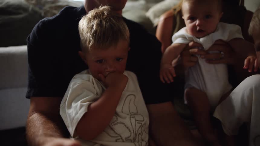 A man sits on a couch with a baby on his lap and the mom next to him holding a baby