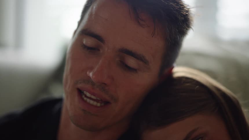 A woman is leaning her head on the shoulder of a man who is talking while looking straight ahead