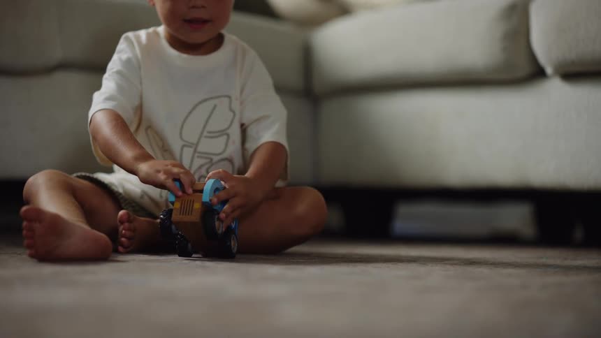 A child sits on the floor and pushes a toy truck on the ground
