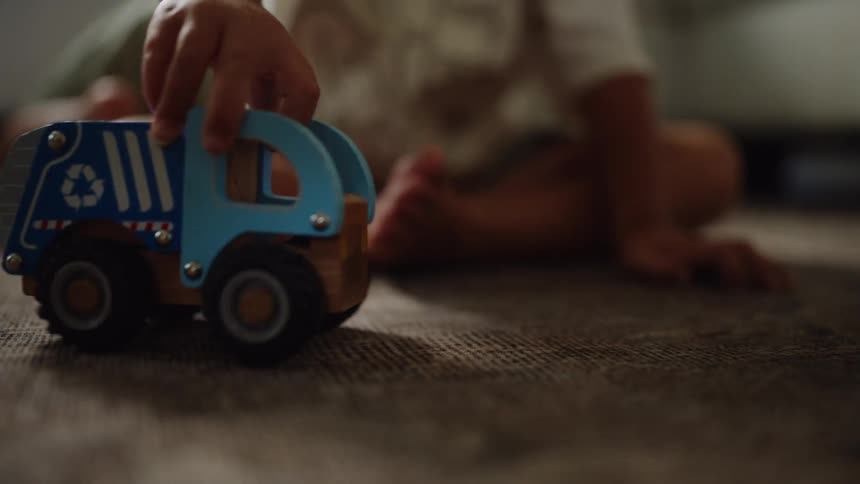 A child on a textured brown carpet is seen in a close view playing with a blue toy truck and pushing it around