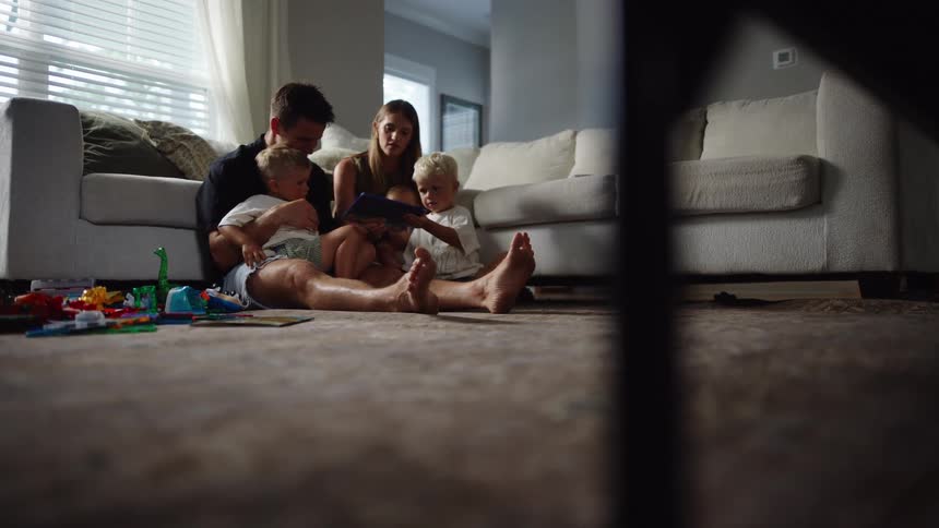 Family sitting on the living room floor reads a book together next to scattered toys