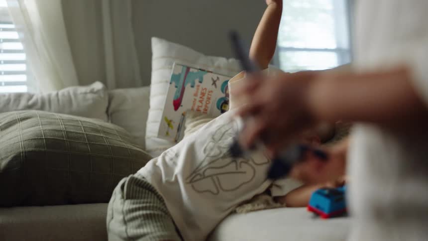Two children play on a couch with one of the children waving a toy airplane and the dad appears to play with them