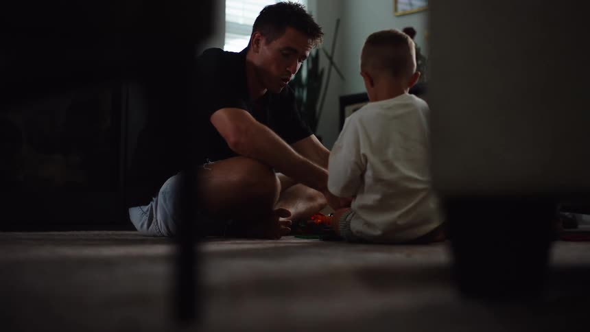The video shows a man and a young boy sitting on the floor in a room playing with toys the man appears to be teaching or guiding the boy as he plays