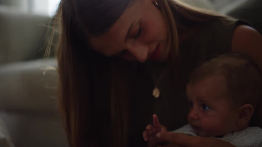 A woman cradles a baby in her arms gently resting her hand on the childs head