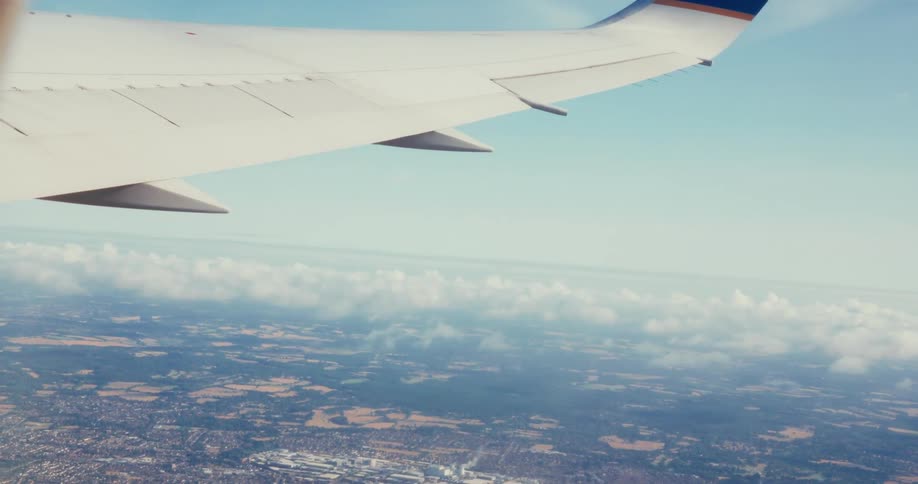 Airplane wing in flight above clouds and landscape below