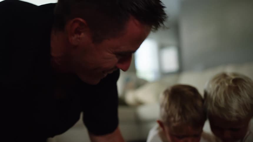 Father and his sons play with toy trucks on the living room floor