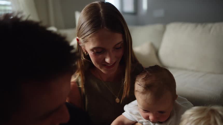 A young woman holding an infant smiles while sitting with her family