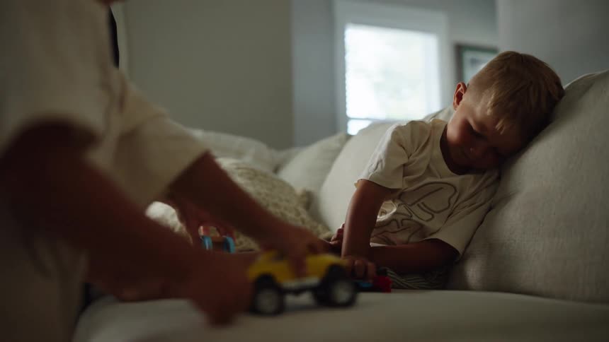 Two children sit on a couch in a room and play with a toy truck