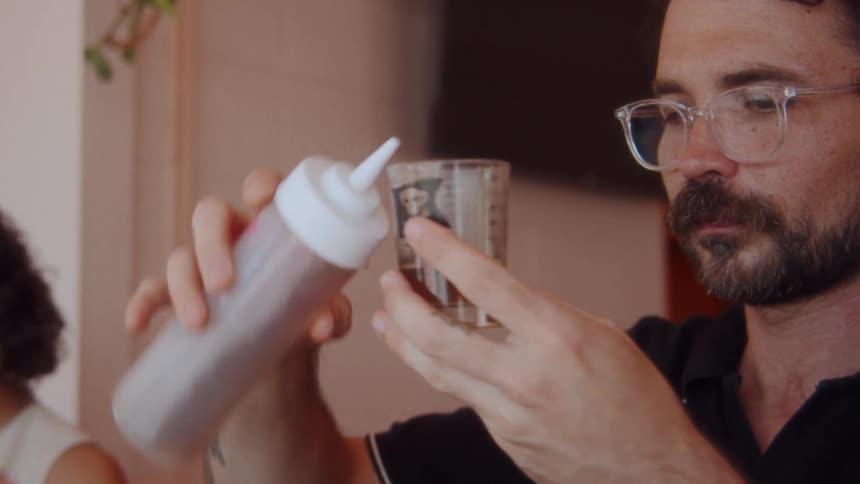 A man in glasses pours a liquid from a squeeze bottle into a glass
