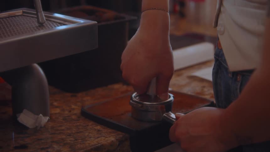 A young man in a caf grinds coffee beans and places them in a coffee machine to make a cup of coffee at midday