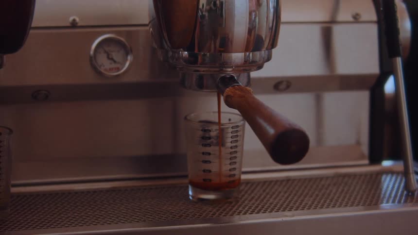 Closeup of espresso pouring into a marked glass from a portafilter