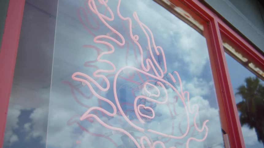 A neon sign shaped like a flame around a flattened yin yang symbol on a store window