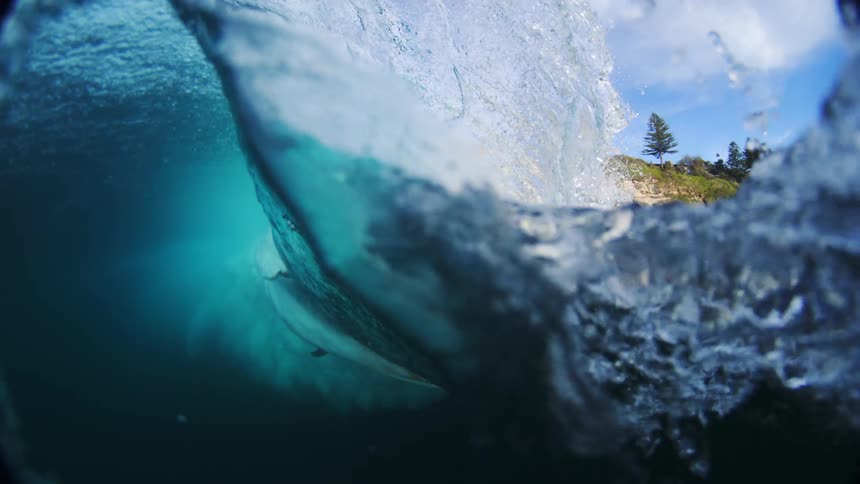 Surfer rides along the face of a big blue wave near a rocky cliff