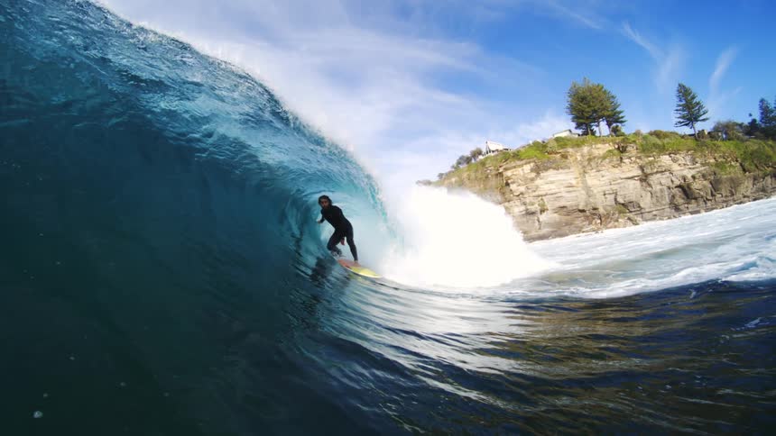 A skilled surfer is riding a large curling wave expertly navigating the bluegreen water the shot captures the dynamic action from within the wave itself with a beautiful coastal cliff and bright blue sky visible in the background