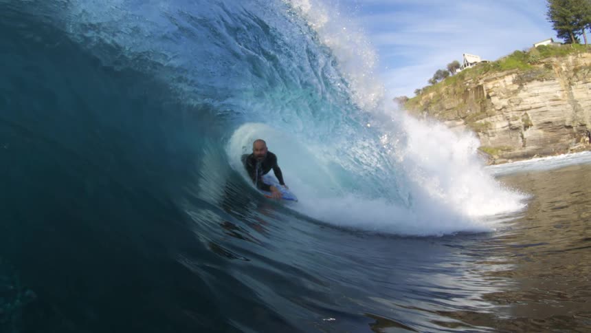 A surfer rides a curling ocean wave under a clear sky