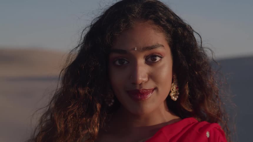 Woman wears a red sari and gold earrings in an outdoor setting