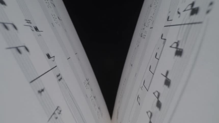 A low angle view looks up at two white pages of sheet music that are held open with black notes and symbols visible on the lines