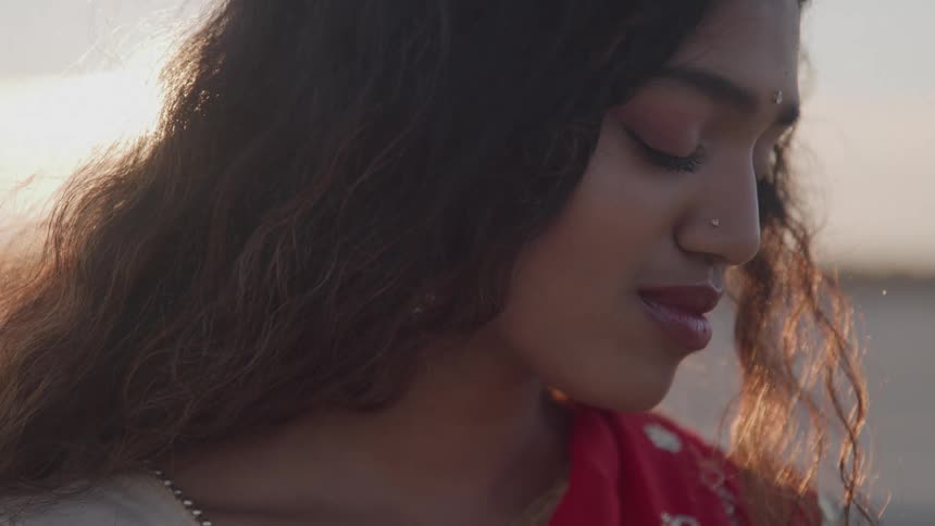 Woman in a red dress looks down softly lit by the setting sun