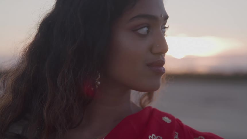 The sun rises behind the woman standing on the sand