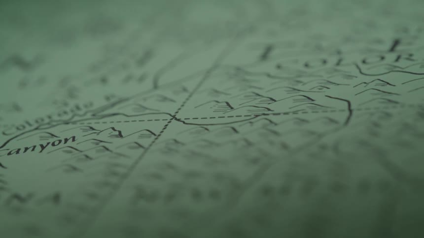 A shot focuses on a vintage map with the names of states like utah and wyoming visible on the paper the camera slowly moves across the map highlighting the detailed drawings of mountains and lakes