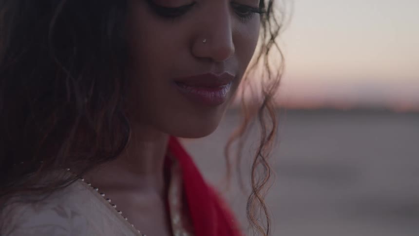 A beautiful woman with long curly brown hair and a piercing in her nose is shown in a closeup shot her eyes are closed and she appears calm and serene with a slight smile on her face