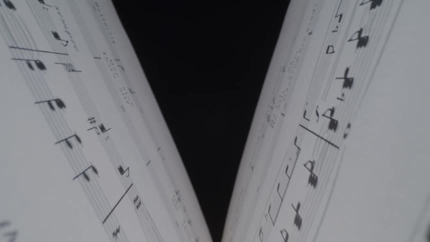 Macro view down the crease of open sheet music creates a soft vshape with musical notes drifting out of focus