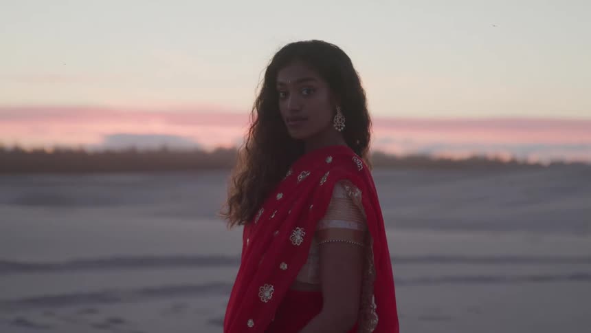 The woman stands on the sand as the sun rises