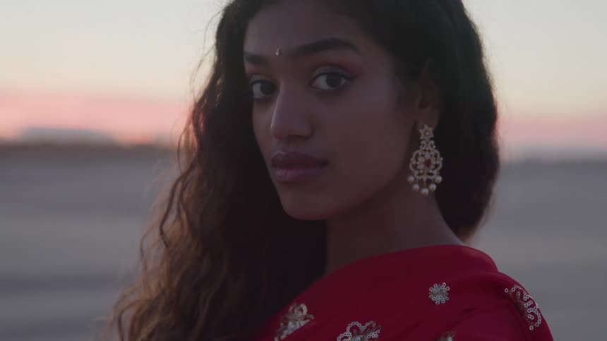 An indian young woman in a red dress with large earrings long hair and a bindi jewel