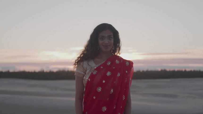 Woman wears a traditional red outfit with golden embroidery at sunset
