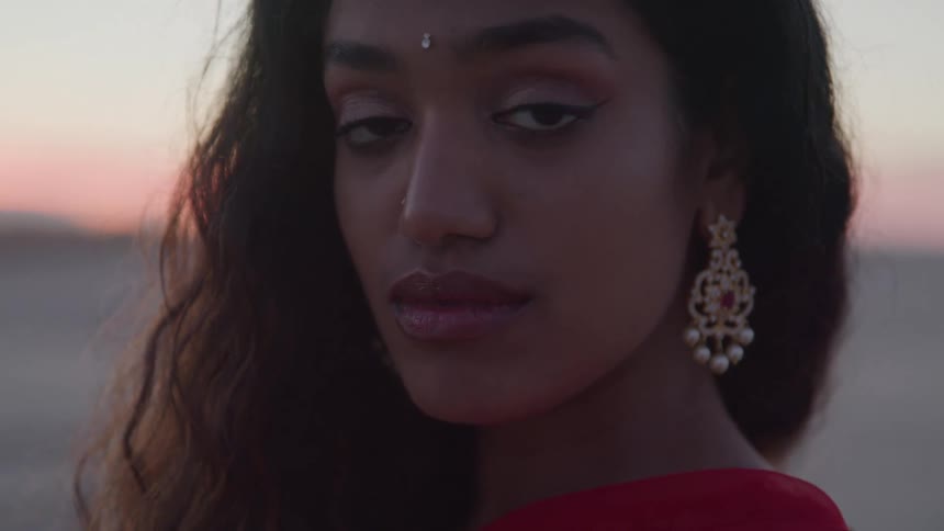 An indian woman in traditional jewelry looks at the camera at sunset