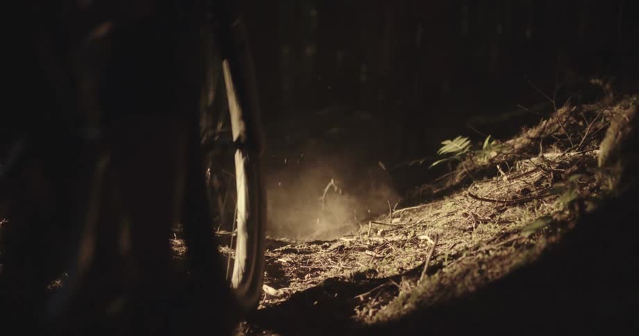 A very low angle shows a persons bike tire on a dirt path in a forest spinning and kicking up dust as the bike moves