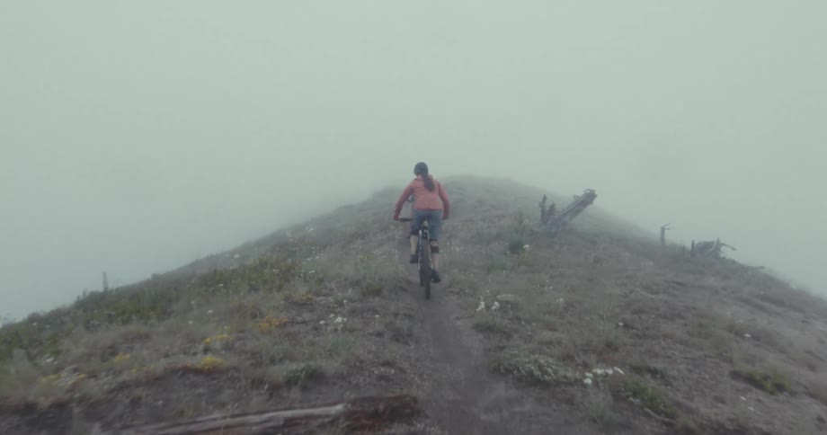 Two people ride bicycles on a dirt path up a hill