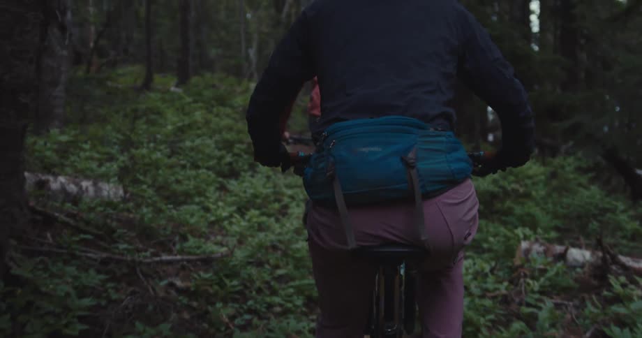 Two young women ride their bicycles through a trail in the woods during daytime