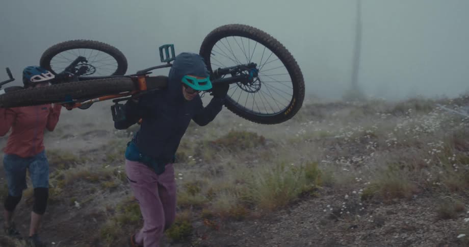 Two people carry their mountain bikes up the hill
