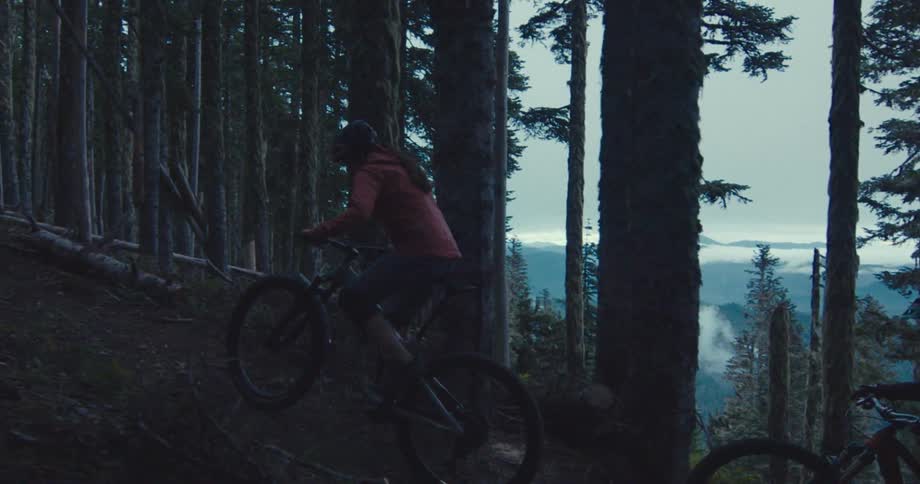 Two women cycling on a mountain surrounded by a forest outdoors