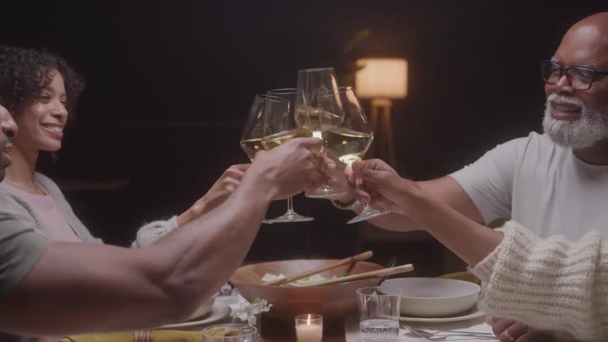 Group of people toast with glasses of white wine around a dinner table