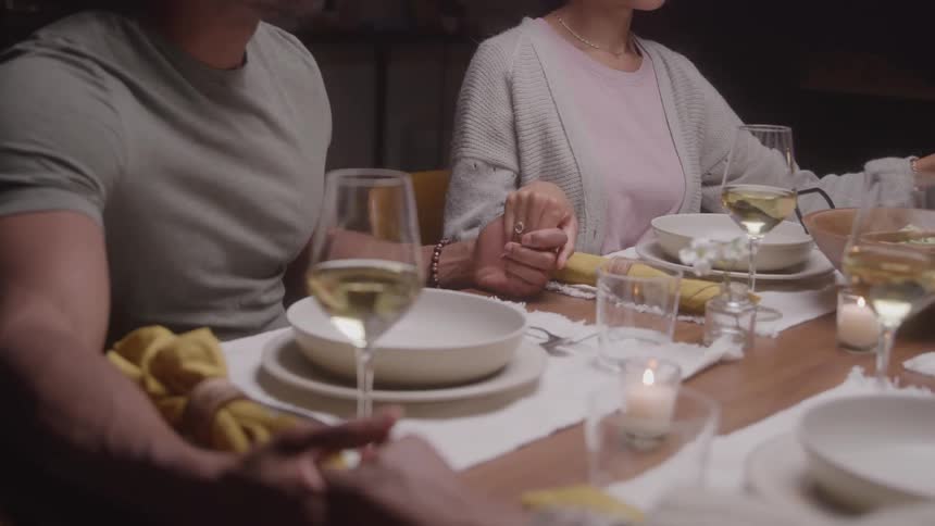 People hold hands around a set table pausing to pray before the meal