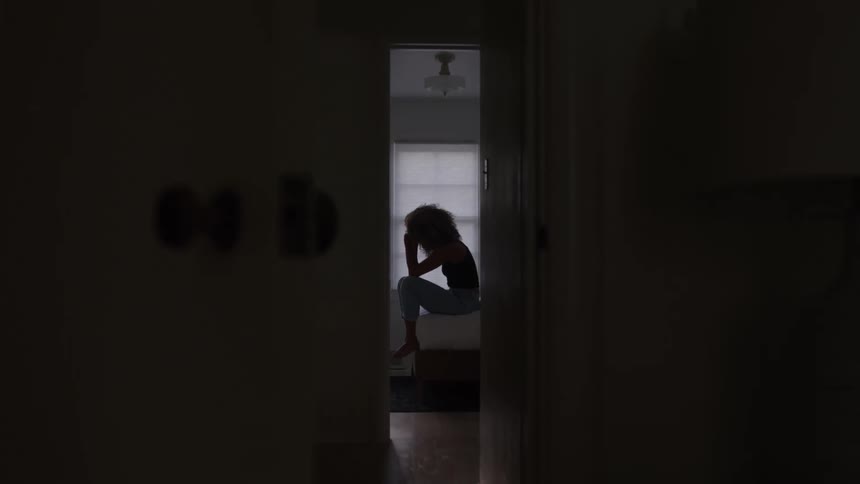 Woman sitting on the bed with her hand on her forehead in a dark room