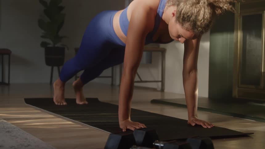 A young woman does multiple push ups atop a mat in her home