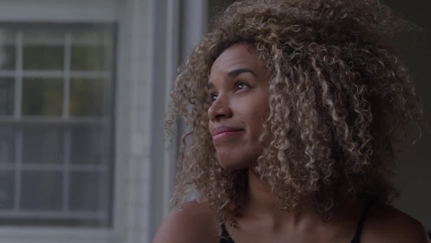 Thoughtful close portrait of a curlyhaired woman gazing out a window in gentle light