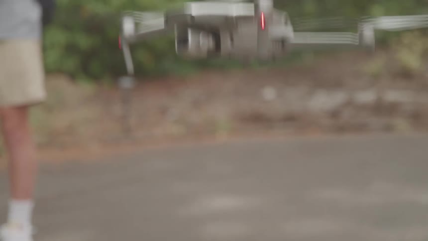 Gray drone flying low with spinning propellers and a red light on
