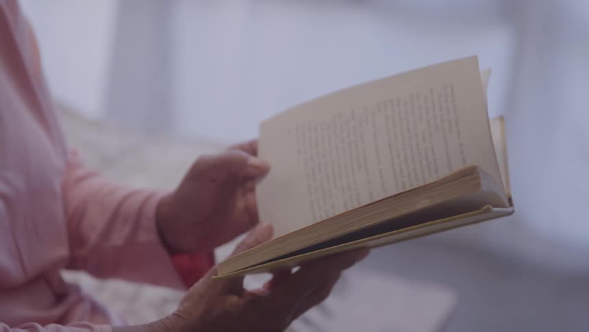 Close up of a young woman flipping through pages of a book while reading in a room during daytime