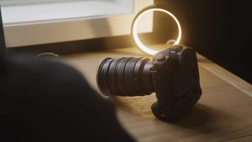 Professional camera with a large lens rests on a table next to a lit ring light