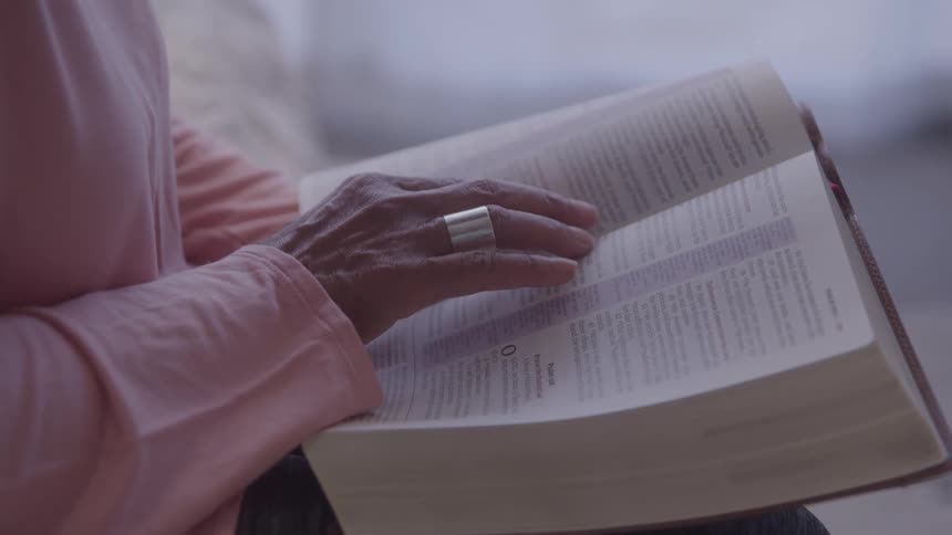 An elderly womans hand following along passages in a large bible