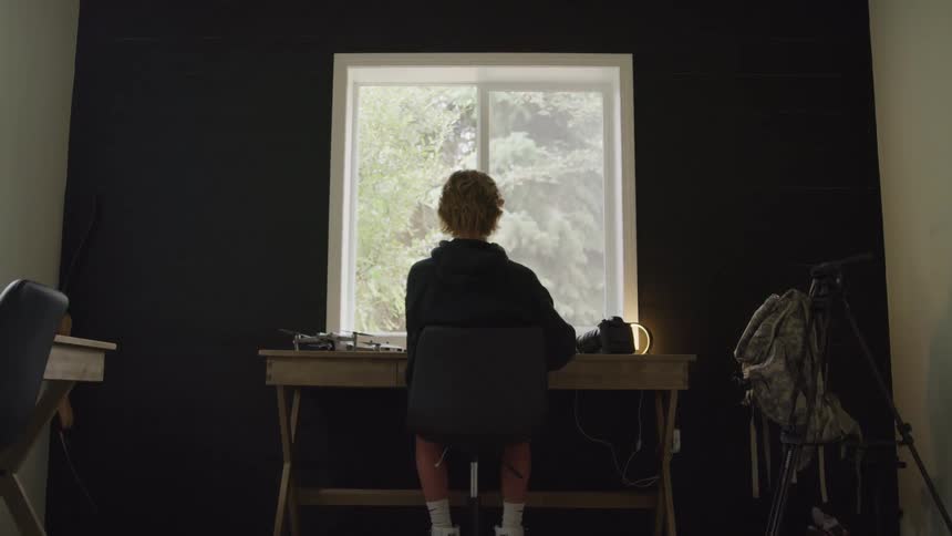 The person is sitting at the desk facing the window