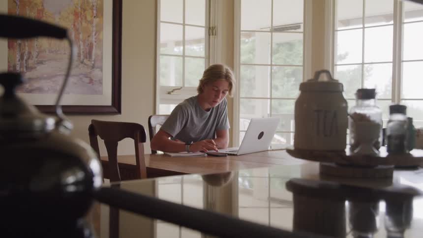 The teenager is using his laptop and writing