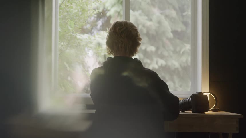 Person sitting at a desk looks out the window beside a camera