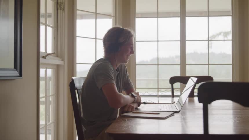 Man sitting at the table attends a video call on his laptop