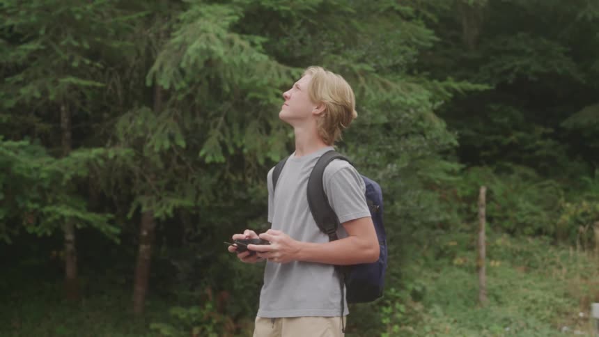 The man is controlling a drone by the forest
